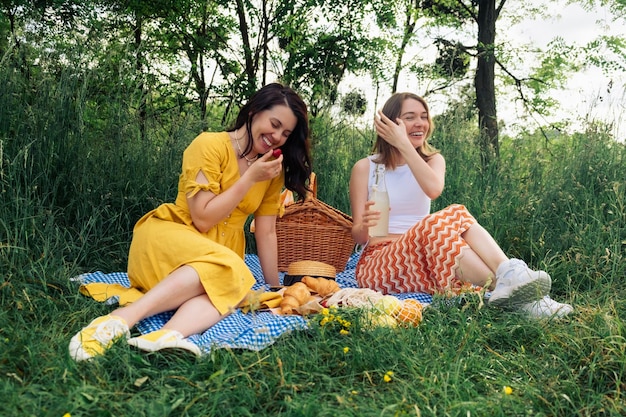Photo two young women laugh on blue blanket at an openair picnic