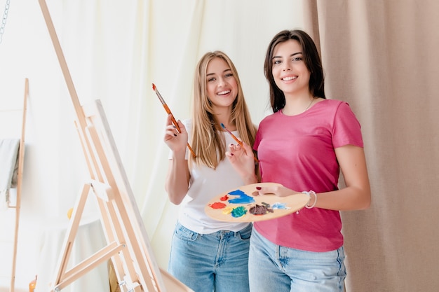 Two young women learning to draw picture on canvas on lesson in art workshop