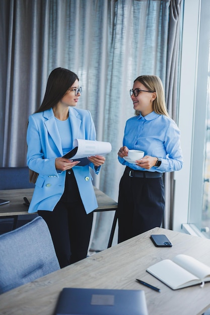 2 人の若い女性マネージャーは、近代的なオフィスで働いています.女性の同僚は、働きながら話しています.フレンドリーなスタッフ