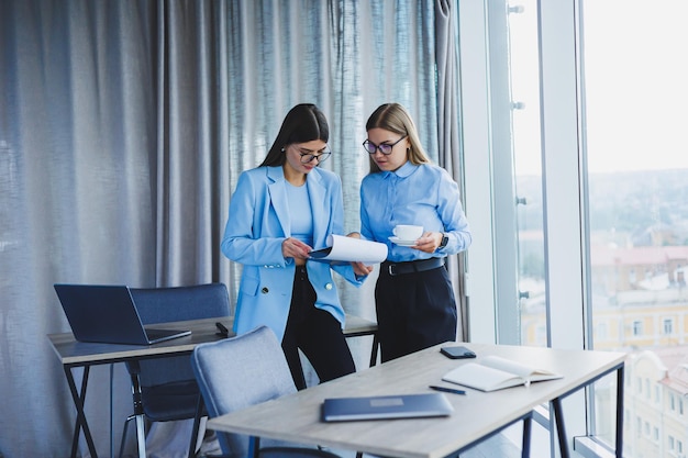 Two young women managers work in a modern office Women colleagues are talking while working Friendly staff