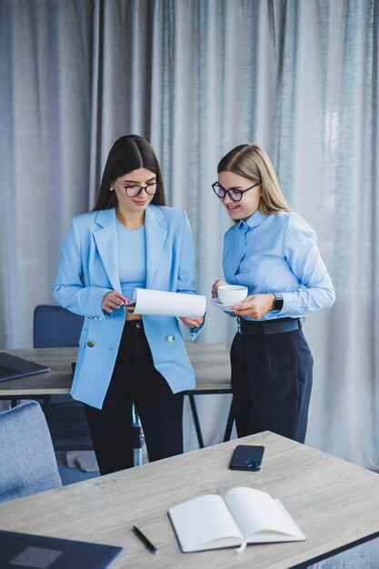 2 人の若い女性マネージャーは、近代的なオフィスで働いています.女性の同僚は、働きながら話しています.フレンドリーなスタッフ