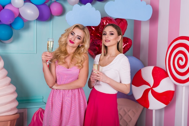 Two young women in pink dresses hold glasses of champagne.