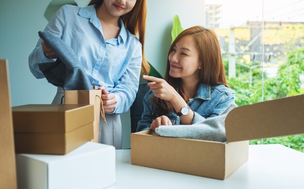 Две молодые женщины получают и открывают дома почтовый ящик с одеждой для доставки и концепции покупок в Интернете