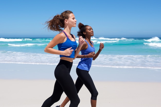 Две молодые женщины, бегущие по пляжу