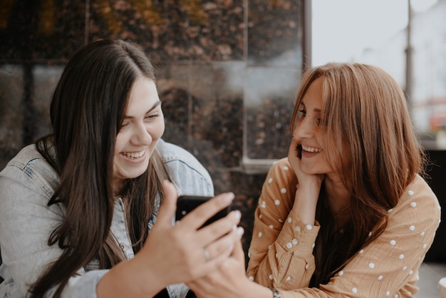 写真 2人の若い女性が電話で市内のオープンカフェに座っています