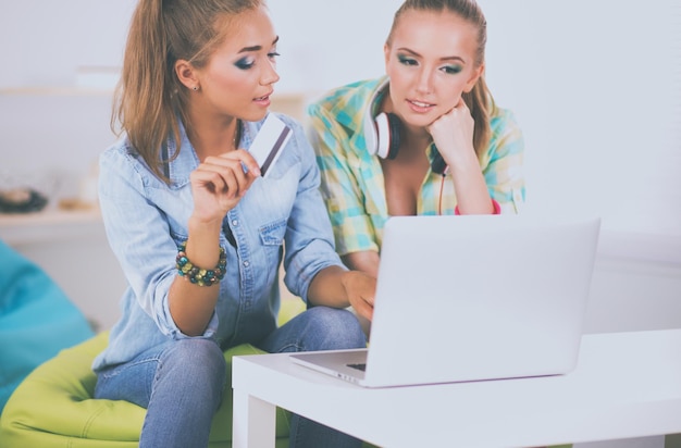 Two young women sitting with laptop and credit cart at home