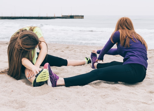 Two young women in sportswear doing stretching on the beach