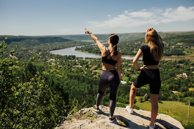 Two young women standing on rock on the mountain and looking at beautiful view