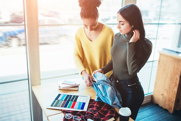 Two young women standing together and working for the same fashion project.