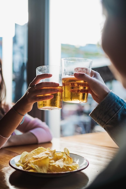 맥주 잔으로 건배하는 두 젊은 여성 테이블에 칩이 있습니다