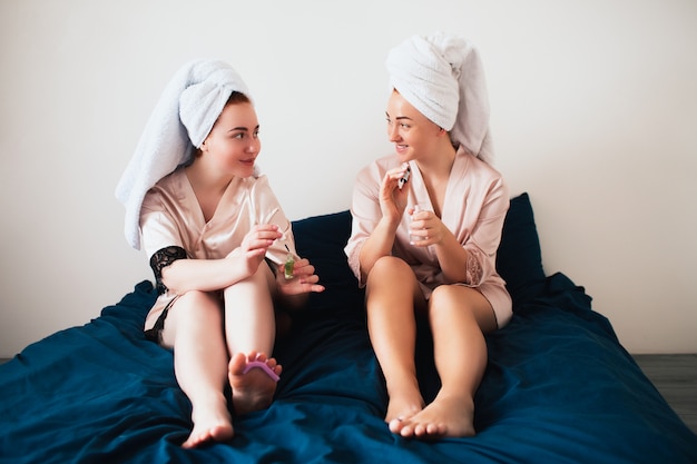 Two young women in towels and pajamas have a fun spa party together in home