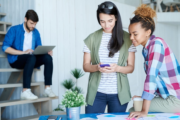 Two Young Women Using Smartphone in Office