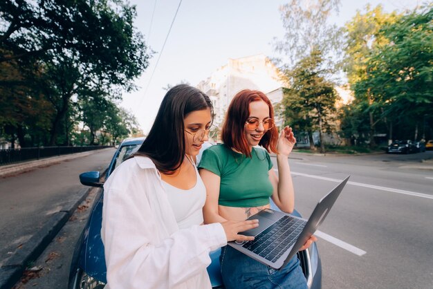 Two young women with a laptop near the car