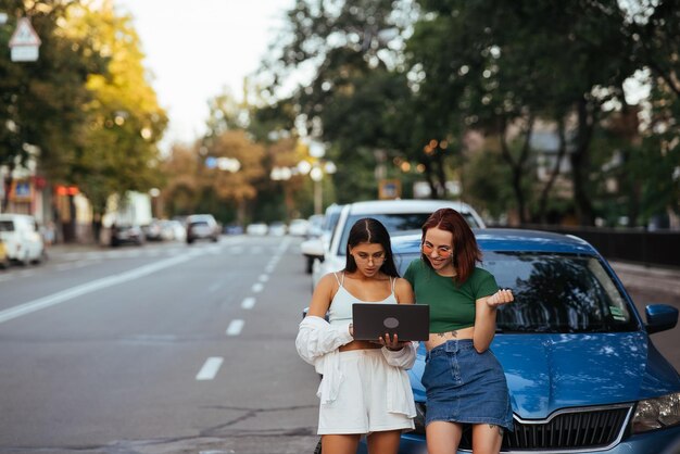 Two young women with a laptop near the car