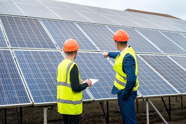 Due giovani lavoratori in tuta e caschi controllano i pannelli solari installati concetto di elettricità verde