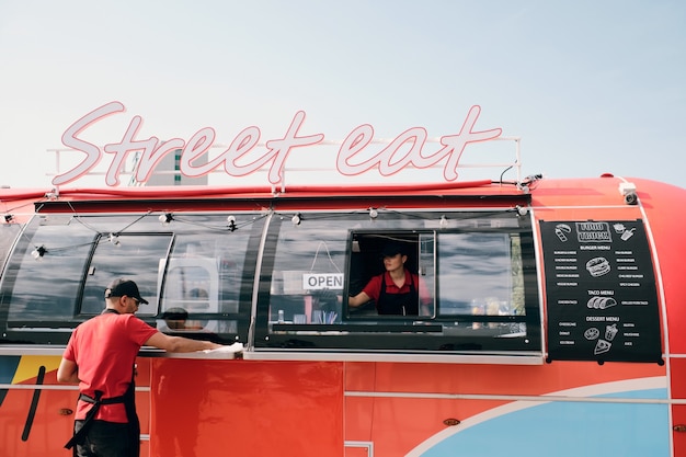 Two young workers in uniform cleaning red food truck