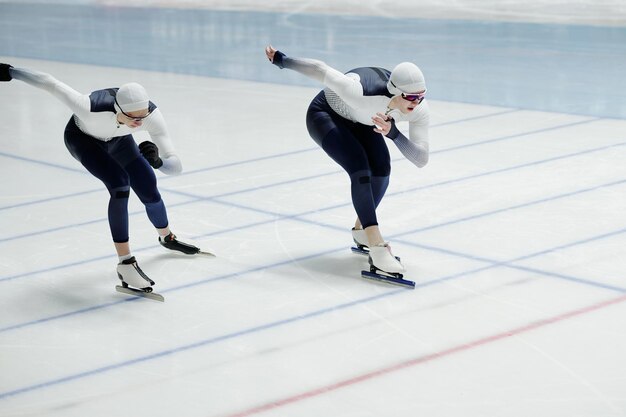 Two ypung male speed skaters in sports uniform moving forwards synchronously