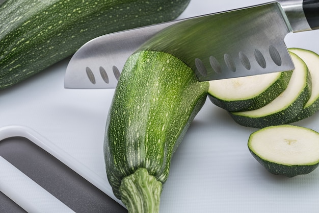 Two zucchini on white plastic board. One squash cut into slices.