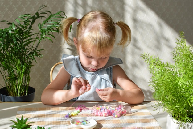 A twoyearold girl is sitting collecting beads from small beads Development of fine motor skills in a child DIY