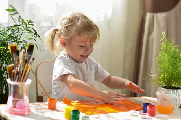 2 歳の女の子がテーブルに座って絵の具で手を汚す 子供の細かい運動能力の発達 手の触覚の発達