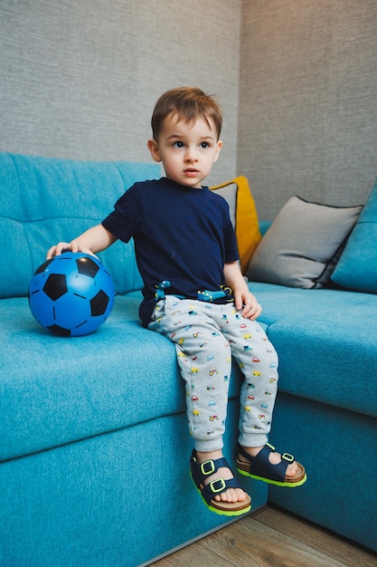 A twoyearold little boy sits on the sofa with a ball in his hands A developed emotional boy plays with a ball at home