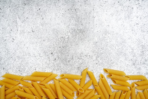 Types of uncooked pasta. Penne pasta uncooked on a light concrete background. . Flat lay, top view, copyspace