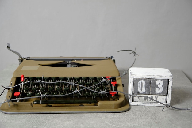 Typewriter is wrapped with barbed wire with wooden calendar next with date May 3Concept Press Freedom Day