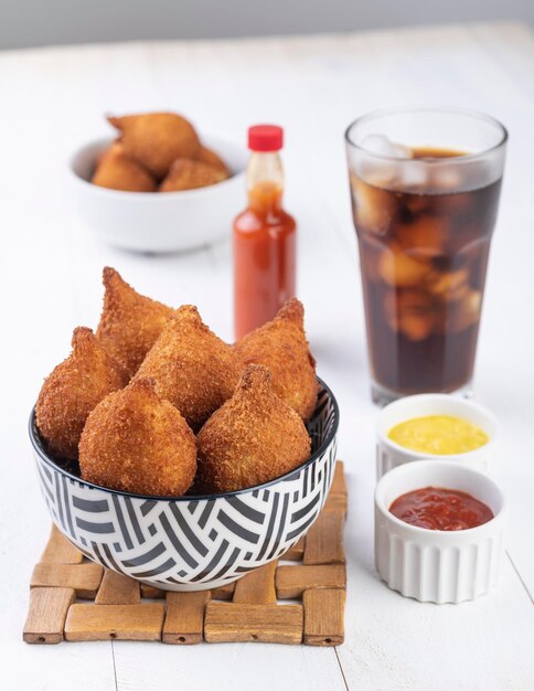 Typical brazilian snack coxinha on a plate with soda glass ketchup pepper and mustard