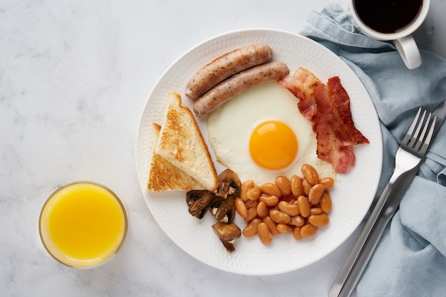 Типичный классический английский завтрак вкусные яйца, бекон, грибы, фасоль и сосиски на тарелке