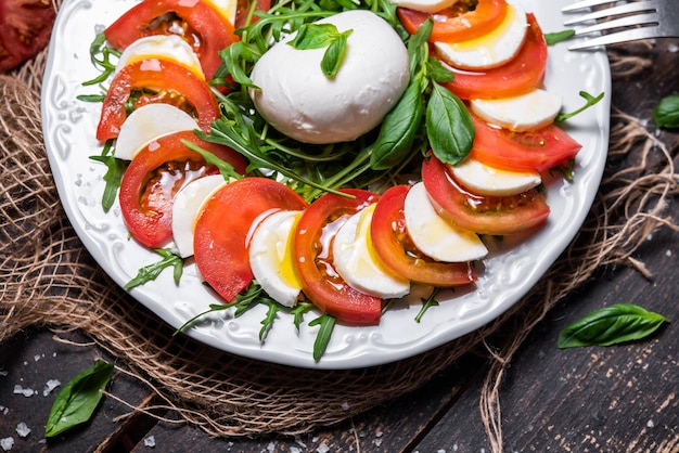 Typical Italian dish of cow or buffalo mozzarella cheese with arugula basil tomato olive oil