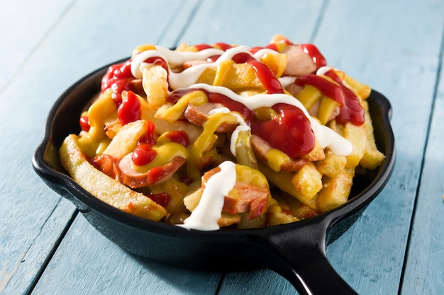 Typical Latin America Salchipapa. Sausages with fries, ketchup, mustard and mayo in iron pan 