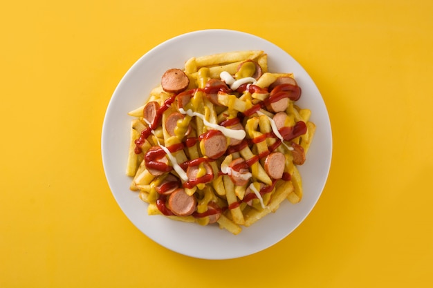 Typical Latin America Salchipapa on yellow surface. Sausages with fries, ketchup,mayo and mustard.