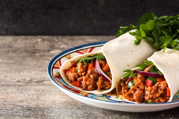 Typical Mexican burrito wrap with beef, frijoles and vegetables on wooden table