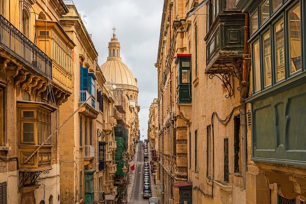 Typical narrow street of Valletta with Cathedral dome, yellow buildings and colorful balconies, Malta, Europe