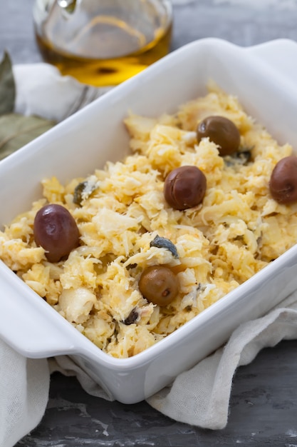 Typical portuguese dish eggs with cod fish and olives in white dish Bacalhau a lisbonense