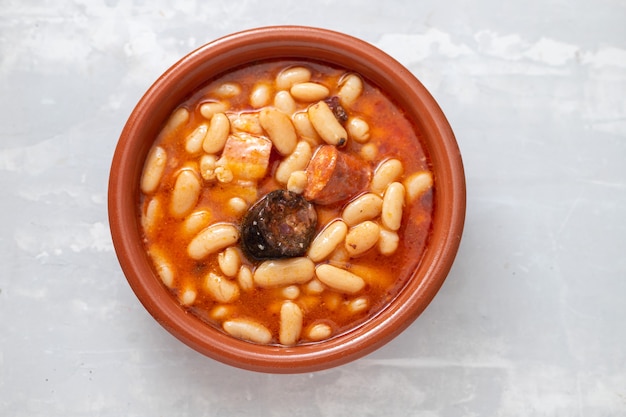 Typical spanish dish fabada, beands with smoked sausages and meat on brown ceramic dish