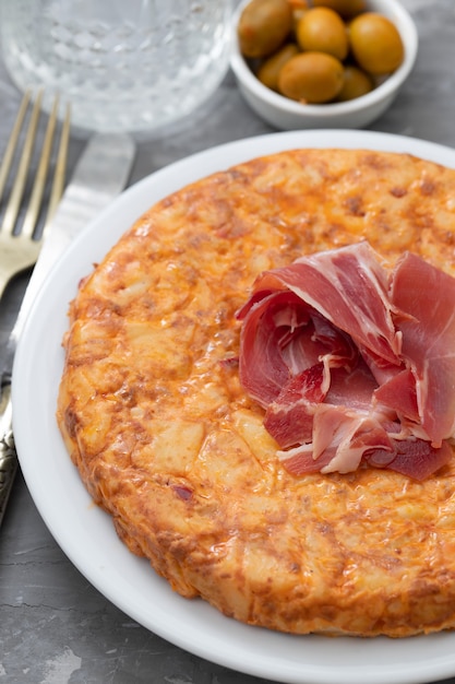 Typical spanish food Tortilla with smoked meat and potato on white dish