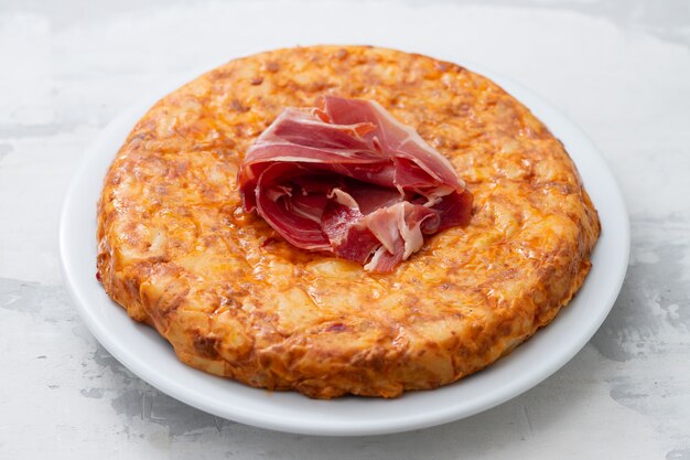 Typical spanish food Tortilla with smoked meat and potato on white dish