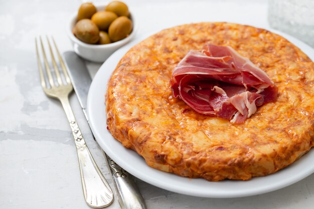 Typical spanish food Tortilla with smoked meat and potato on white dish