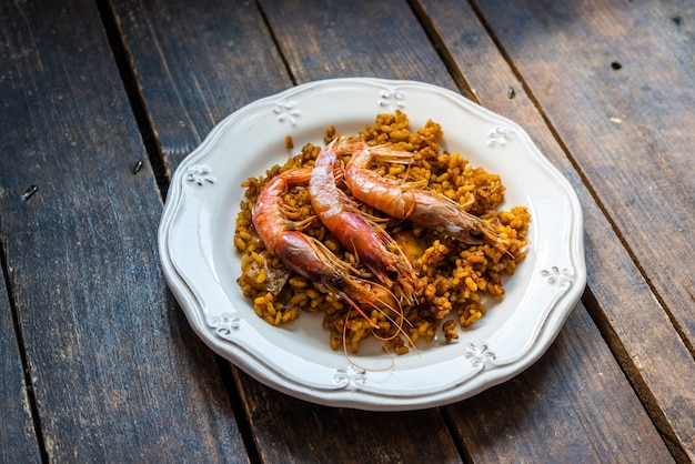 typical Spanish paella with rice and seafood with three prawns on top in an old white plate