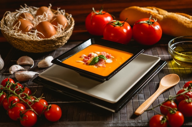 Typical spanish recipe for cordovan salmorejo in a square plate with some ingredients around on a wooden table.
