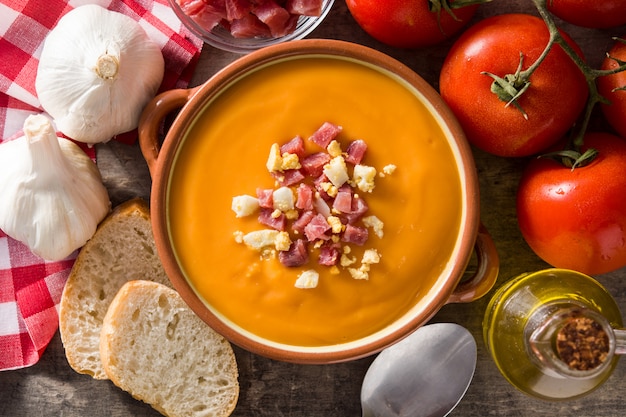 Typical Spanish salmorejo cream with ham and egg on wooden table, top view