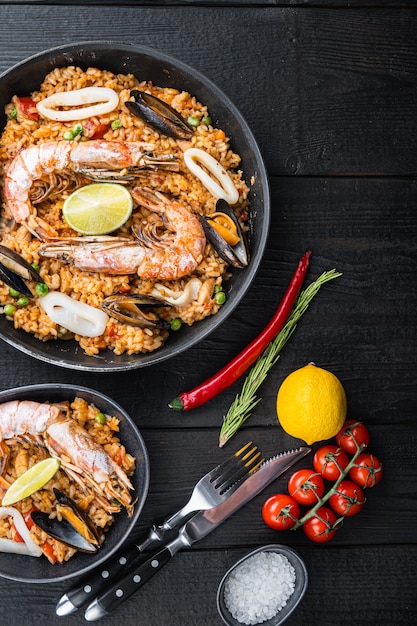 Typical spanish seafood paella in traditional pan and black bowl on black wooden background,