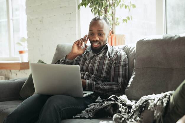 Typing text and talking on phone. Man, freelancer during the work in home office while quarantine. Young businessman at home, self isolated. Using gadgets. Remote work, coronavirus spread prevention.