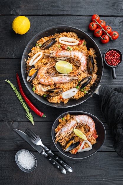 Typische spaanse zeevruchtenpaella in traditionele pan en zwarte kom op zwarte houten ondergrond, plat gelegd, voedselfoto.