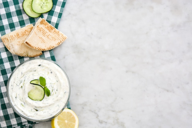 Tzatziki in bowl and ingredients on white marble top viewcopy space