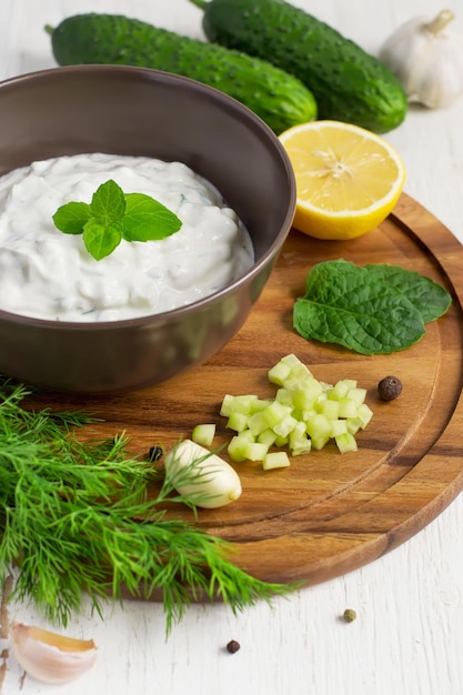 Tzatziki-saus in een kom en ingrediënten - gesneden komkommer, munt, dille, citroen, knoflook