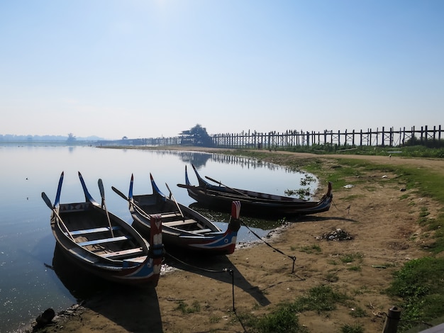 Photo u bein bridge and colorful wooden rowing boats on bank of lake with birds and blue sky