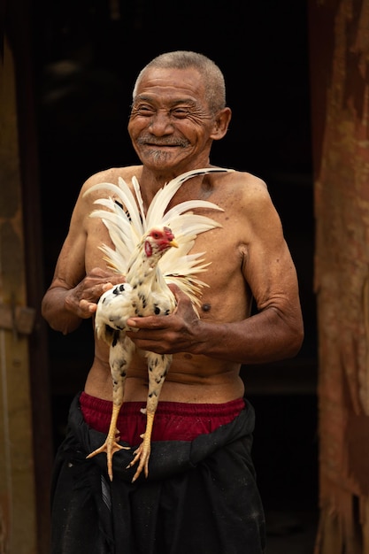 Ubud Bali Indonesia 08012019 Portrait of a grandfather with a rooster Selective focus