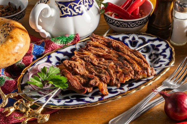 Uch - panja of mutton. Lamb and lamb ribs marinated with spices and fried on the grill on three skewers on an Uzbek plate with red onions and fresh herbs.